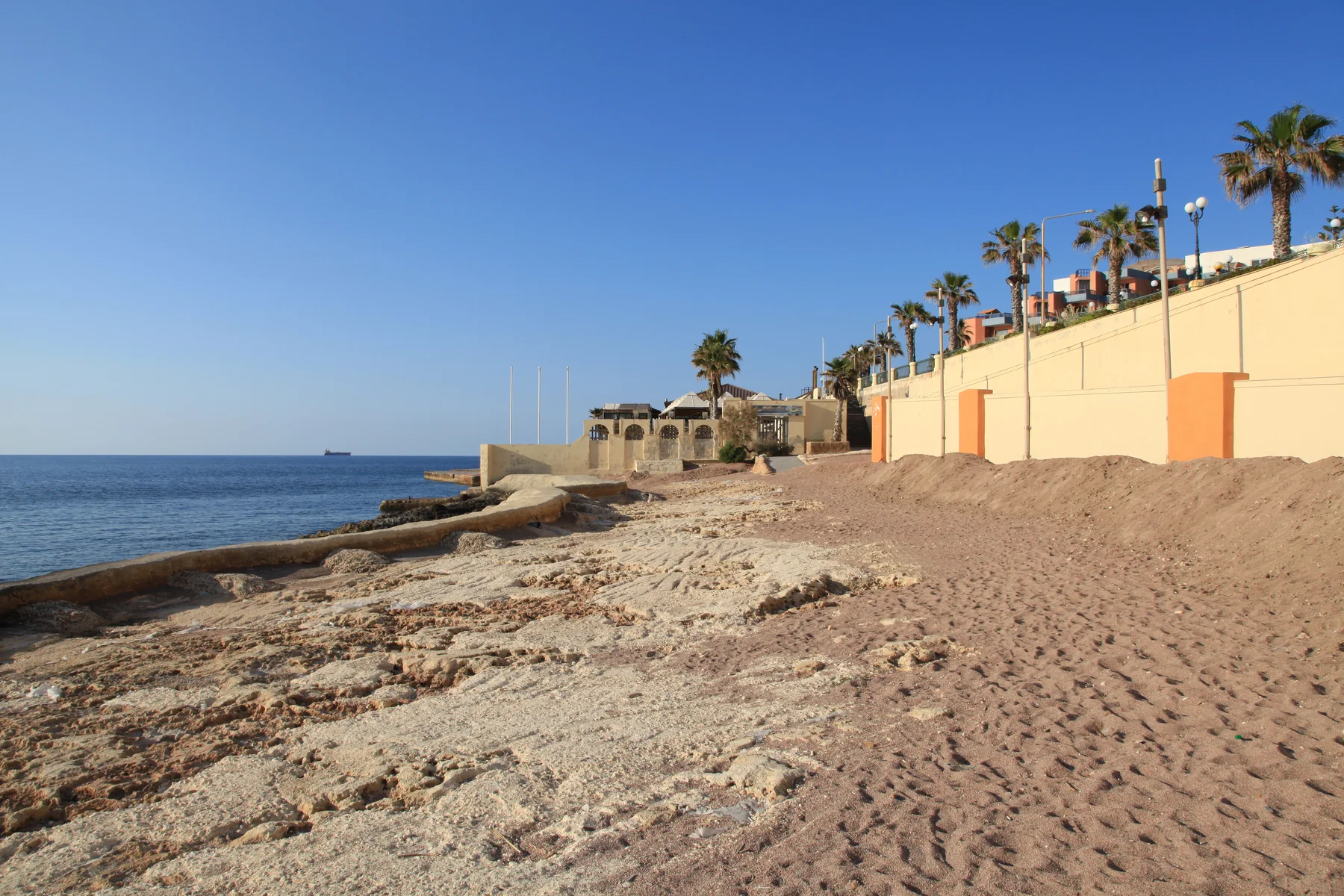Rocky Buġibba shoreline, sea and palm-lined built edge photographed in 2014