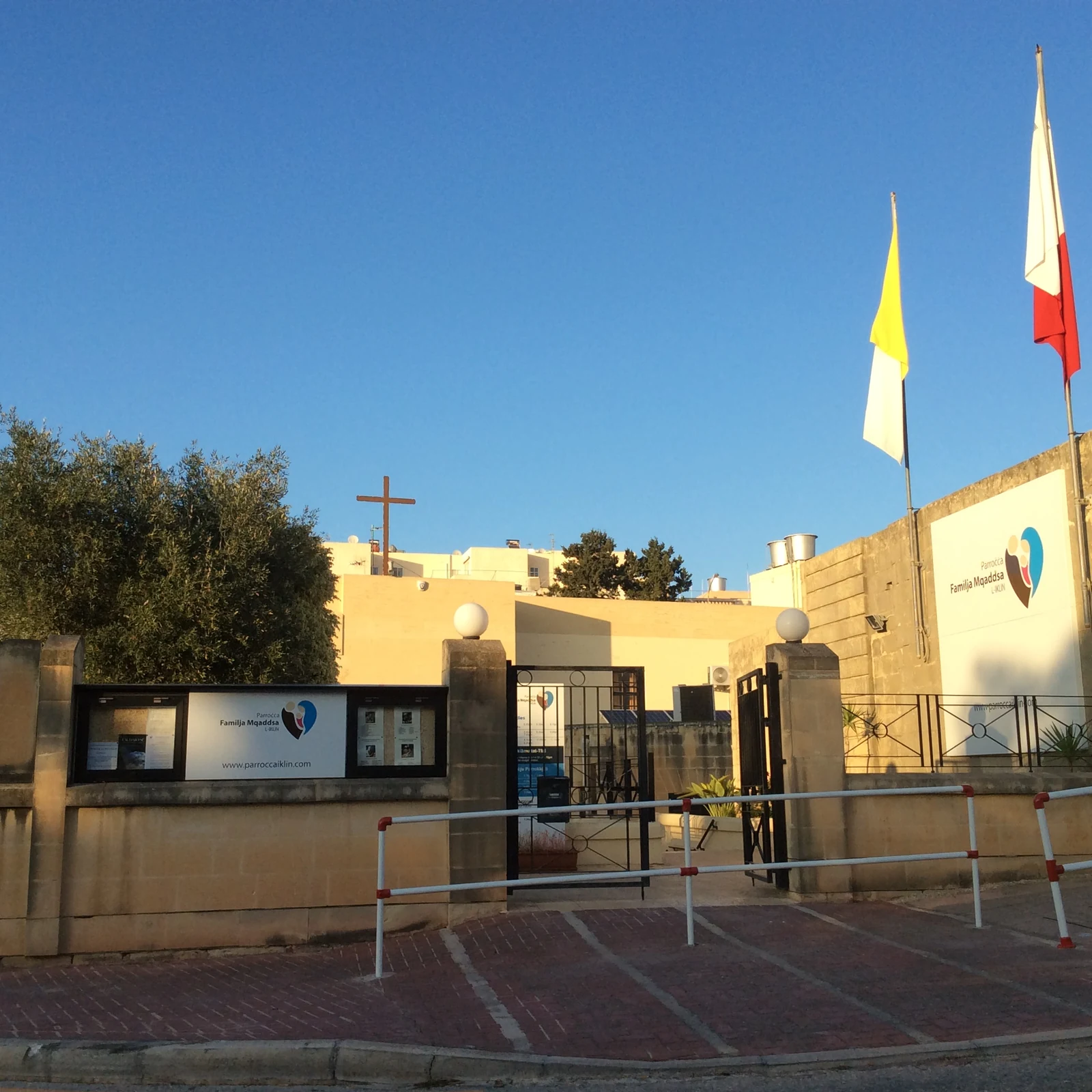 Iklin parish centre with an olive tree, cross and flags
