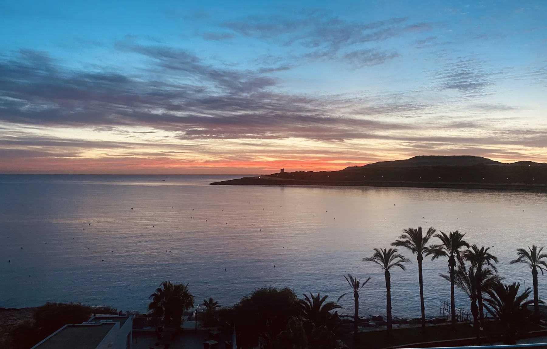 Qawra coastline at sunset with open water, palms and a distant headland