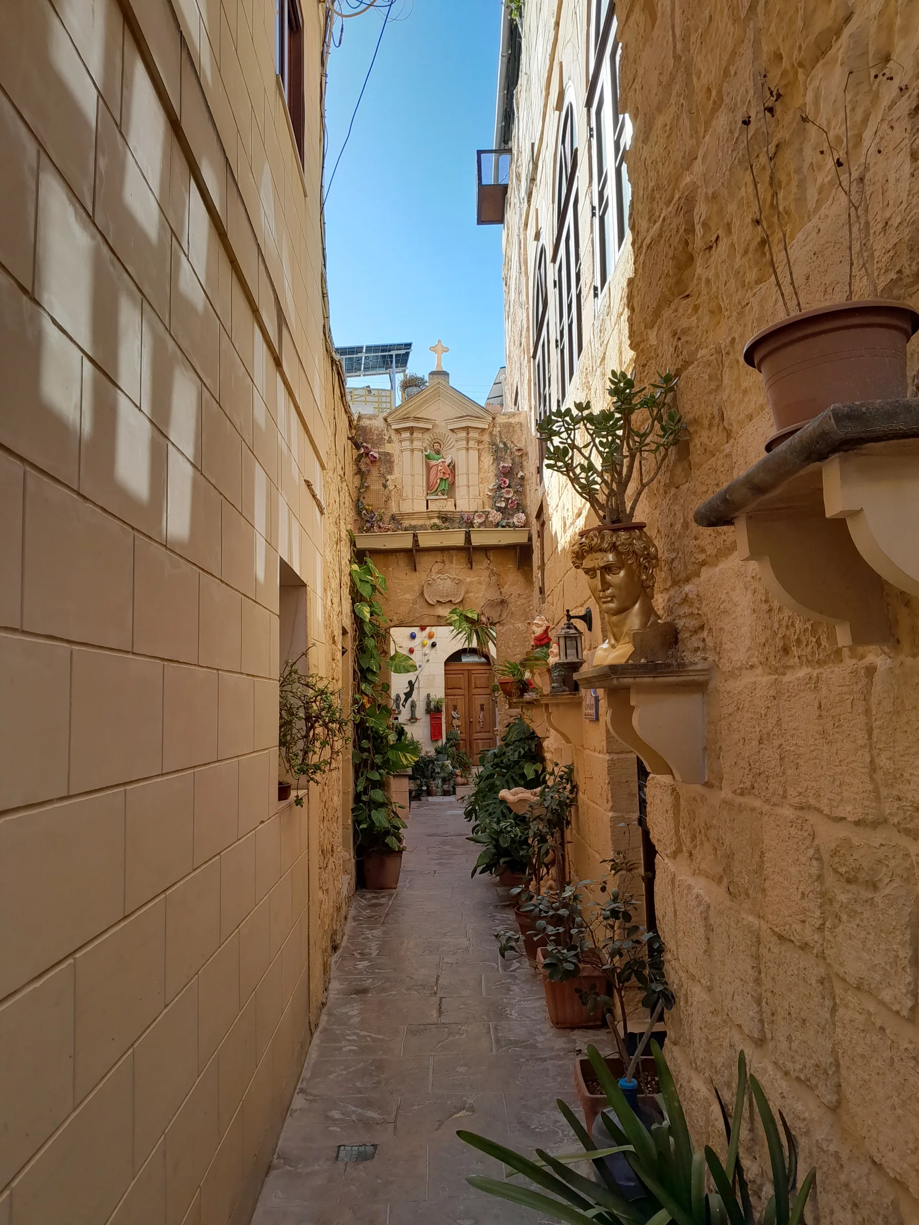 A limestone residential lane in Rabat with planted pots and a decorated religious niche