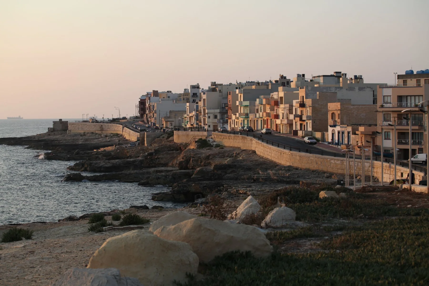 Xgħajra waterfront, rocky shoreline and homes in warm morning light